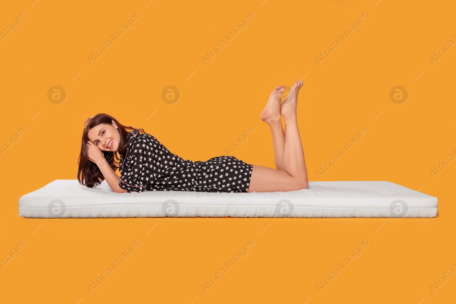 Photo of Young woman lying on soft mattress against orange background