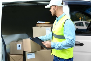 Photo of Young courier checking amount of parcels in delivery van, outdoors
