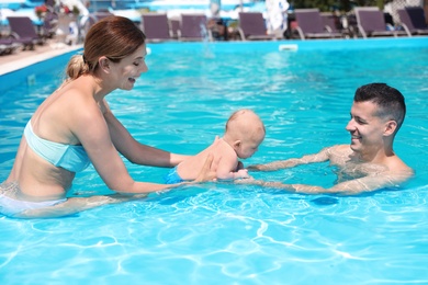 Photo of Happy parents with little baby in swimming pool on sunny day, outdoors