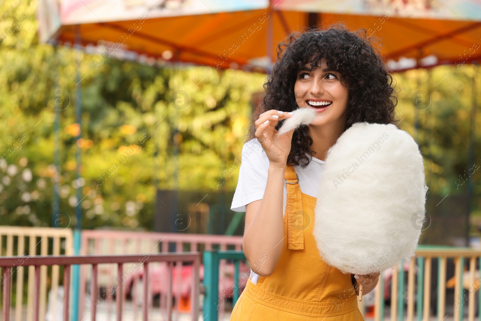 Photo of Beautiful woman eating cotton candy outdoors. Space for text