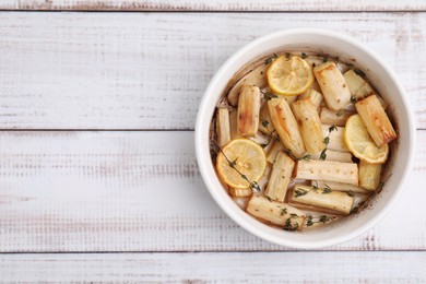 Photo of Dish with baked salsify roots, lemon and thyme on white wooden table, top view. Space for text