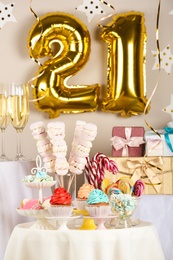 Dessert table in room decorated with golden balloons for 21 year birthday party