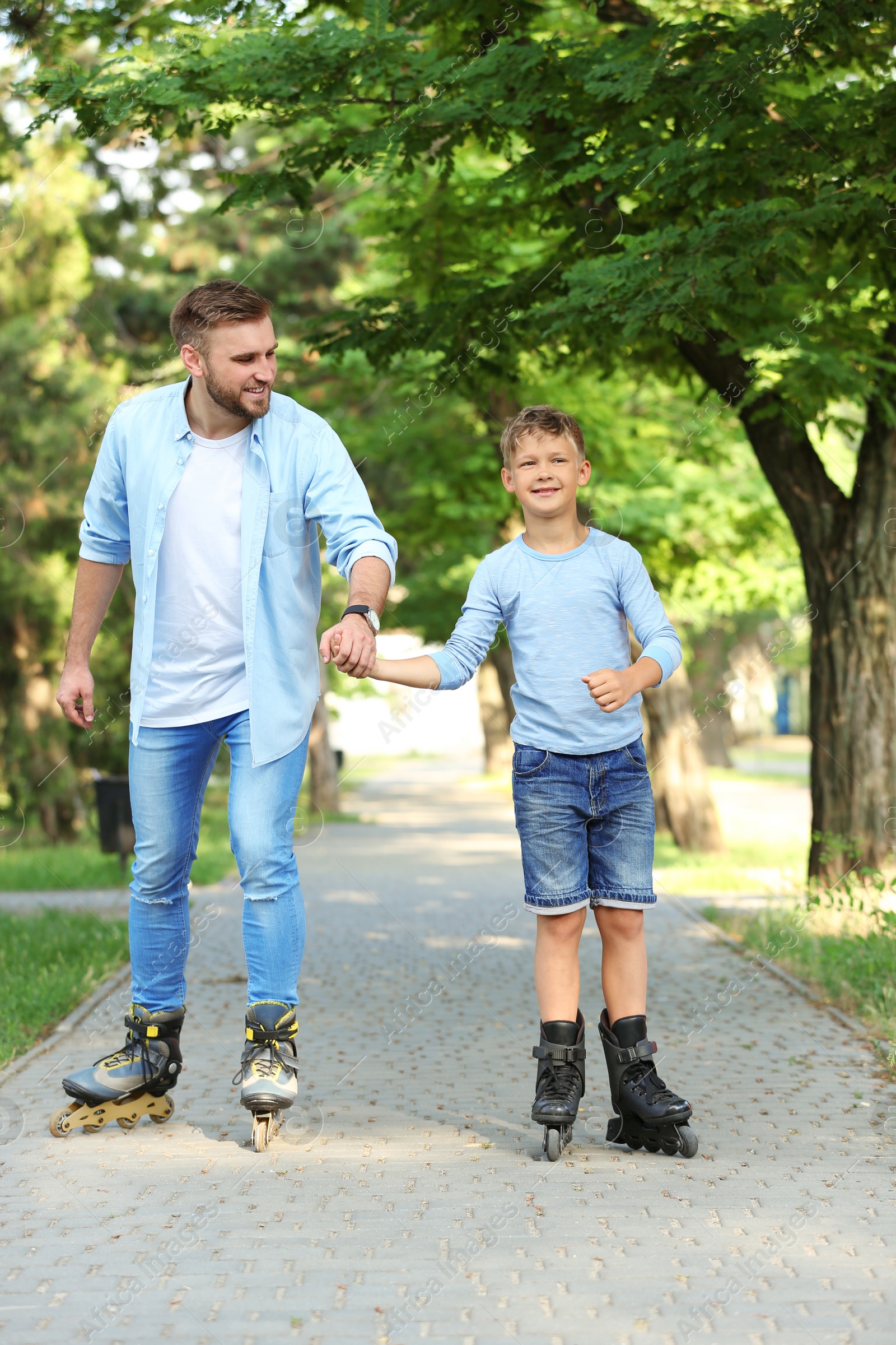 Photo of Father and son roller skating in summer park