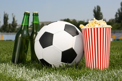 Photo of Football ball with beer and popcorn on green field grass in stadium