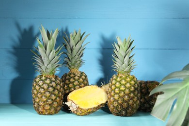 Photo of Whole and cut ripe pineapples on light blue wooden table