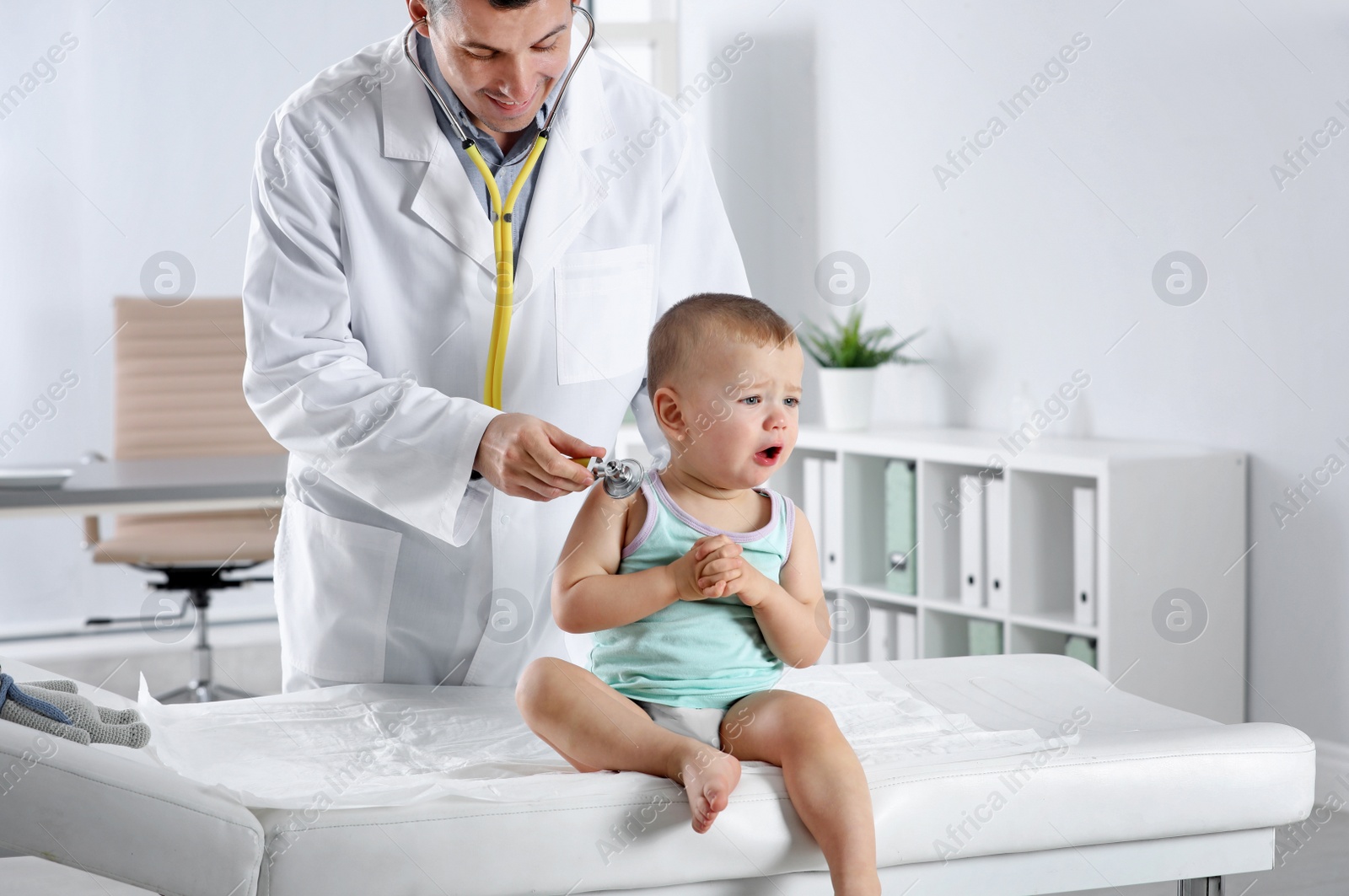 Photo of Children's doctor examining little boy with stethoscope in hospital. Space for text