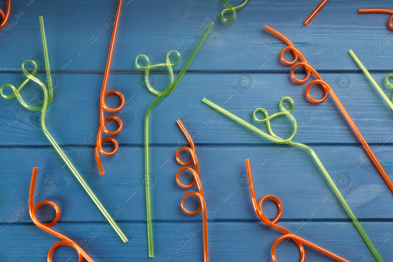 Photo of Colorful plastic drinking straws on blue wooden table, flat lay