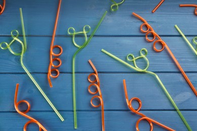 Photo of Colorful plastic drinking straws on blue wooden table, flat lay