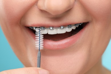 Woman with dental braces cleaning teeth using interdental brush on light blue background, closeup