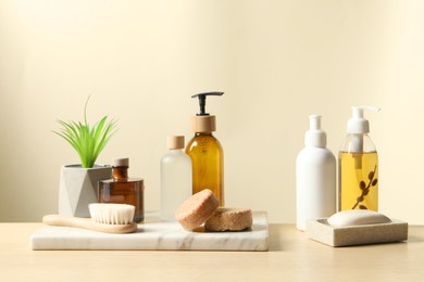 Different bath accessories and houseplant on wooden table against beige background