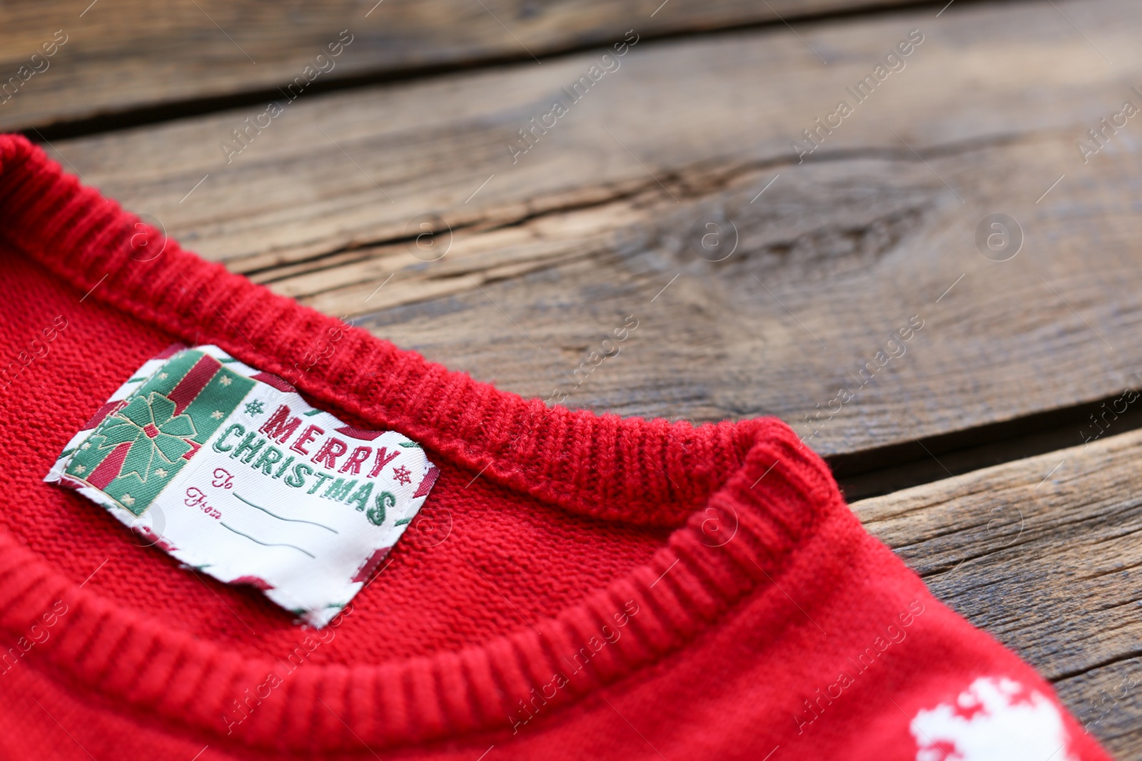 Photo of Christmas sweater with tag on wooden background, closeup