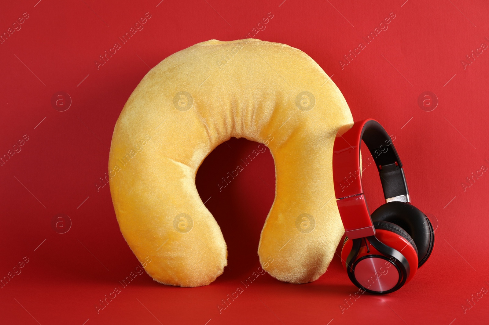 Photo of Yellow travel pillow and headphones on red background