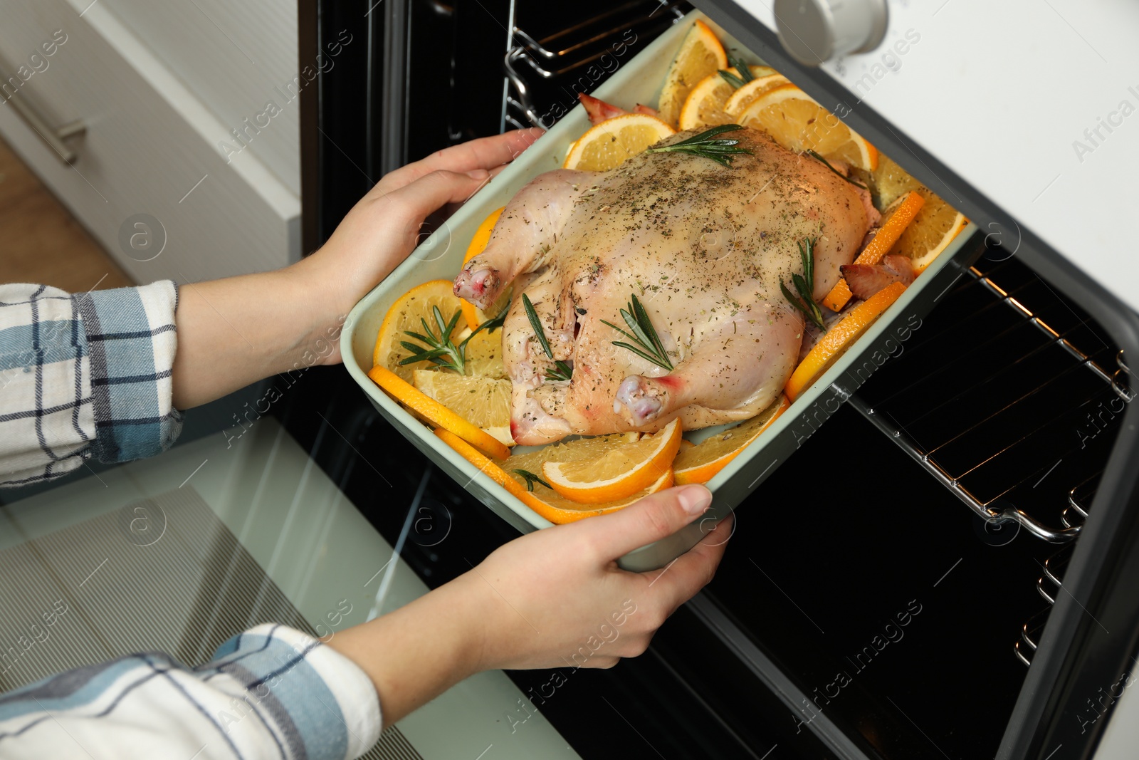 Photo of Woman putting chicken with orange slices into oven, closeup