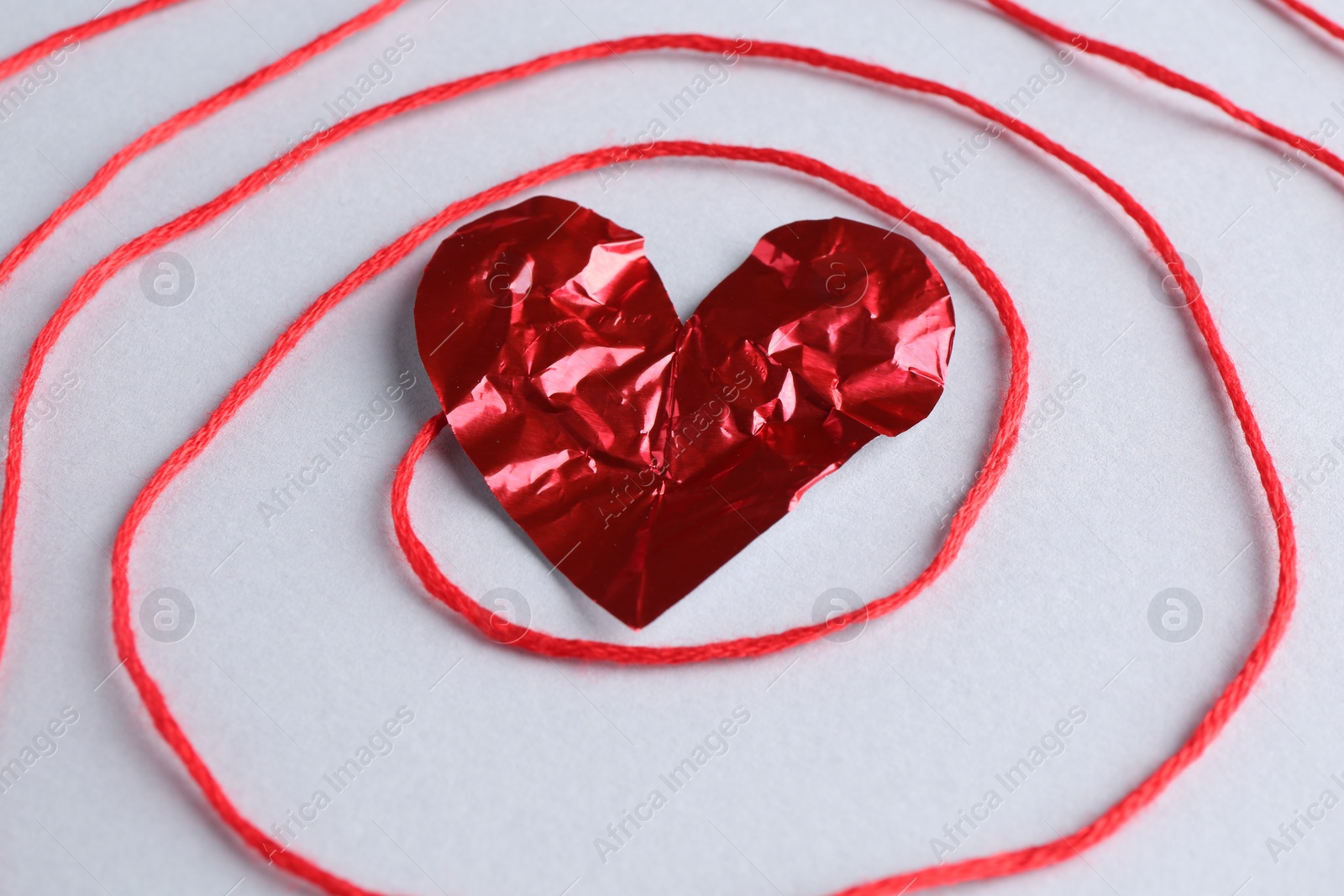 Photo of Red crumpled paper heart and thread on gray background, closeup