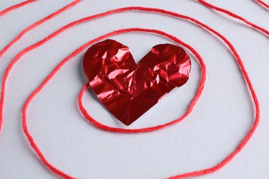 Red crumpled paper heart and thread on gray background, closeup