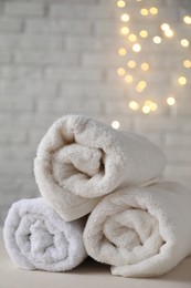 Photo of Rolled terry towels on white table near brick wall indoors