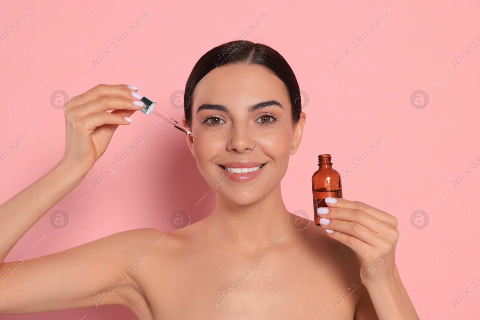 Photo of Young woman with bottle of essential oil on pink background