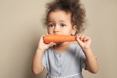 Photo of Cute African-American girl eating carrot on color background