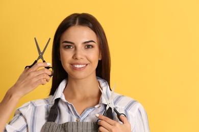 Photo of Young hairstylist holding professional scissors on color background, space for text