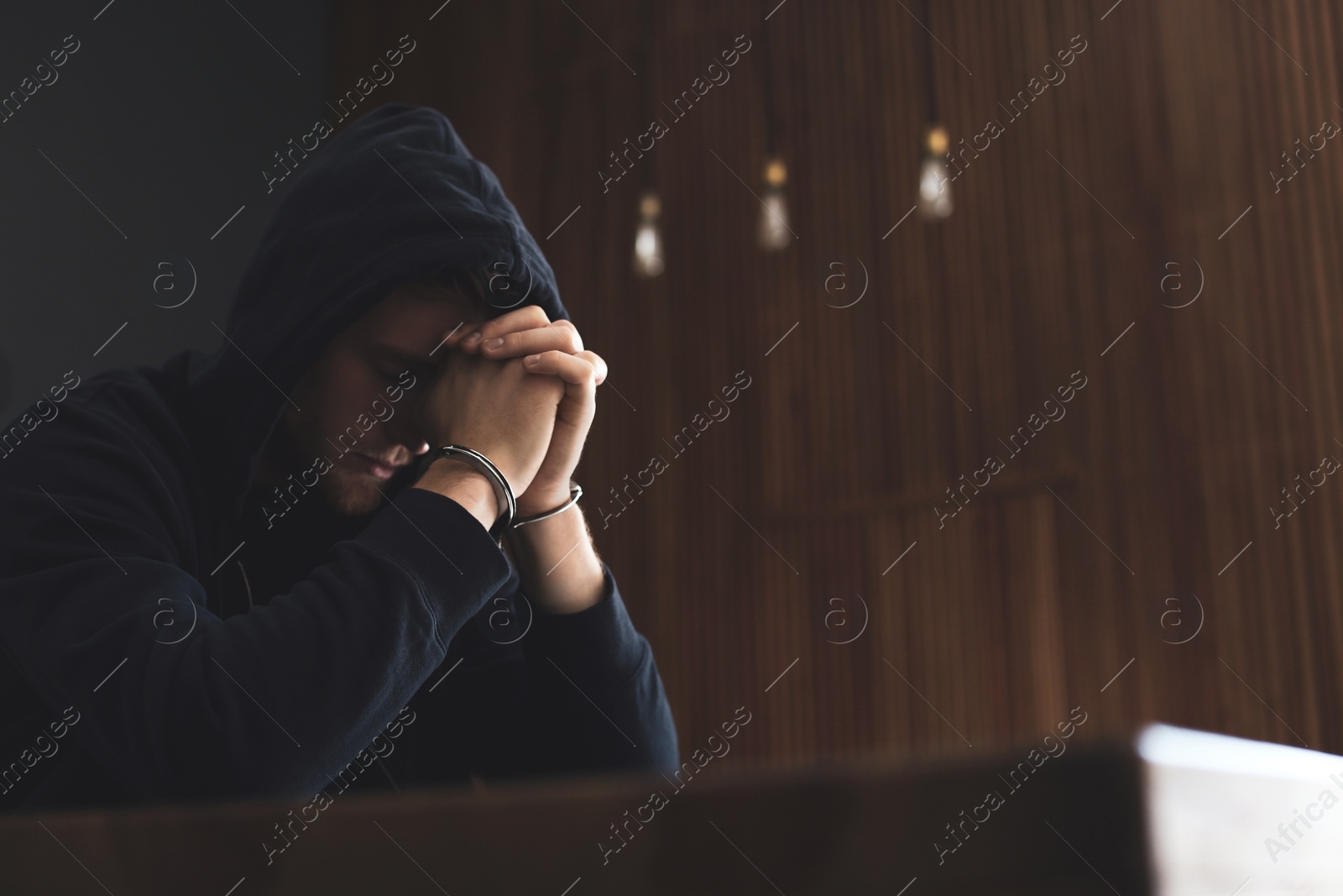 Photo of Man detained in handcuffs at table indoors, space for text. Criminal law