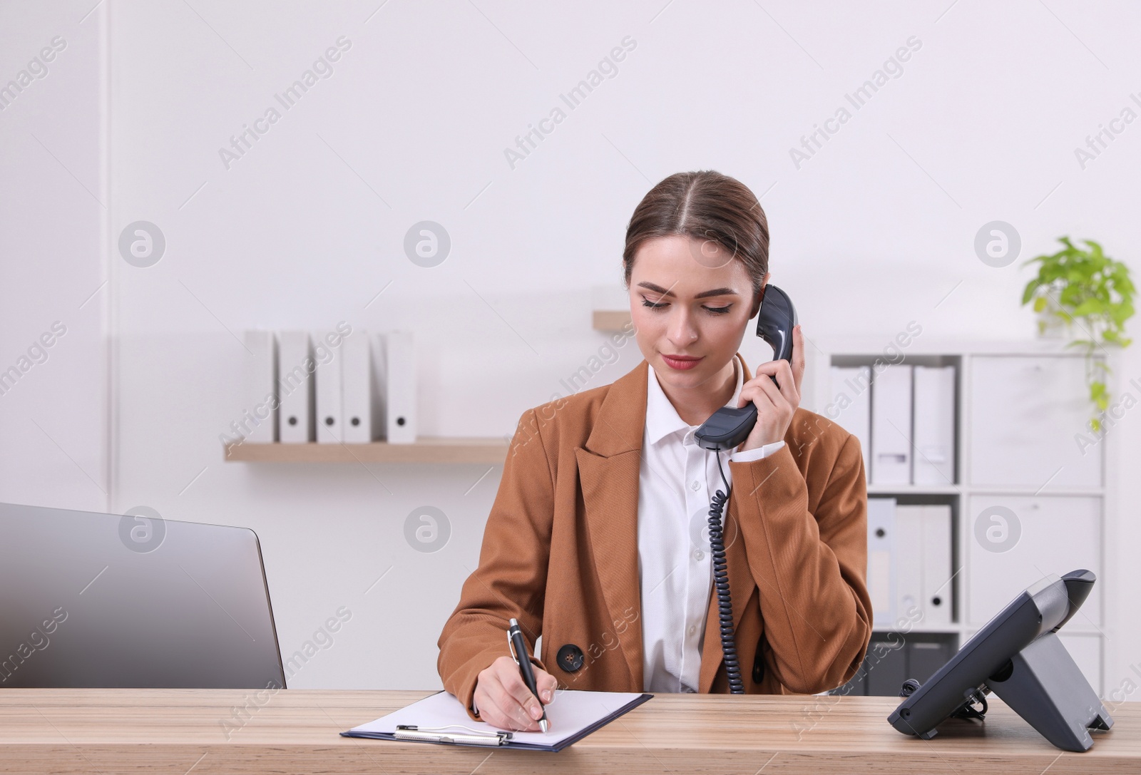 Photo of Female receptionist with clipboard talking on phone at workplace