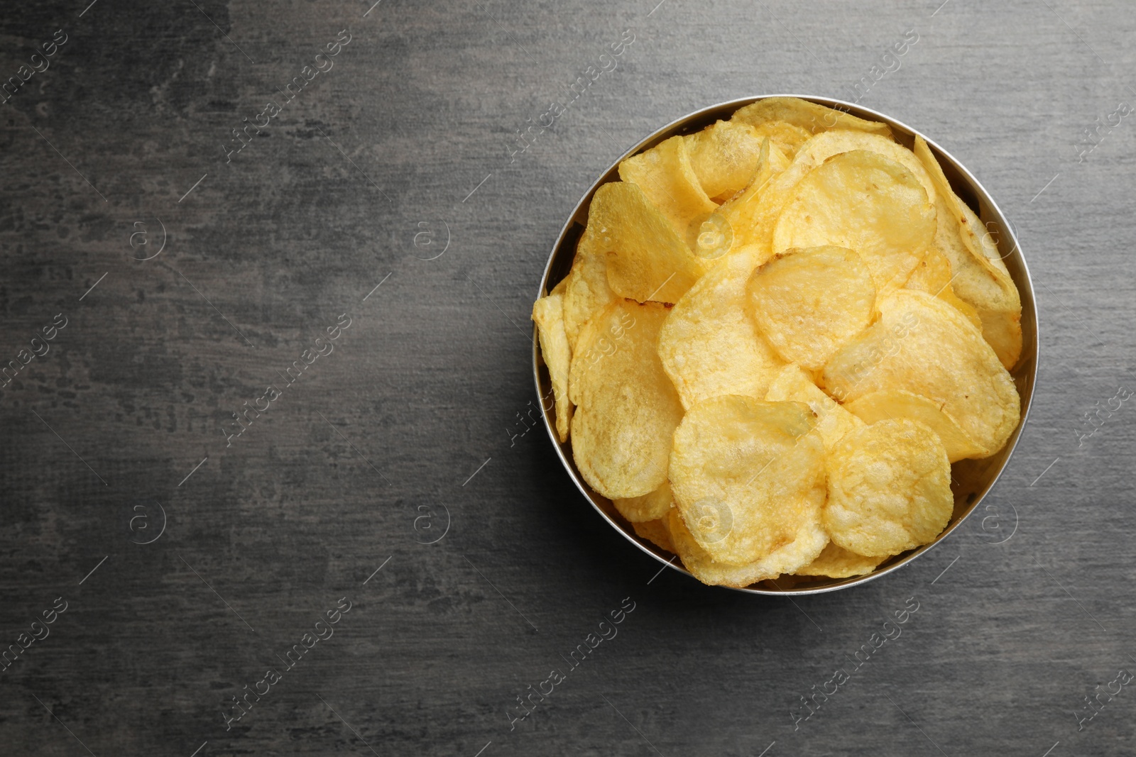 Photo of Delicious crispy potato chips in bowl on table, top view with space for text