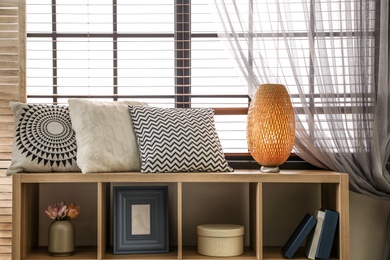 Pillows and lamp on cabinet in room near window. Stylish interior elements