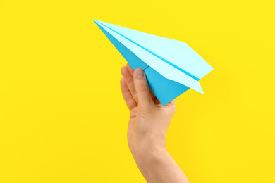 Woman holding paper plane on yellow background, closeup