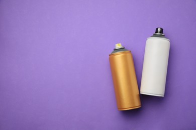 Photo of Cans of different graffiti spray paints on violet background, flat lay. Space for text