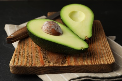 Photo of Halves of delicious ripe avocado on dark table, closeup