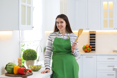 Photo of Young woman with apron and spatula in kitchen