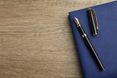 Beautiful fountain pen and blue notebook on wooden table, top view. Space for text