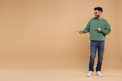 Happy young man pointing at something on beige background, space for text