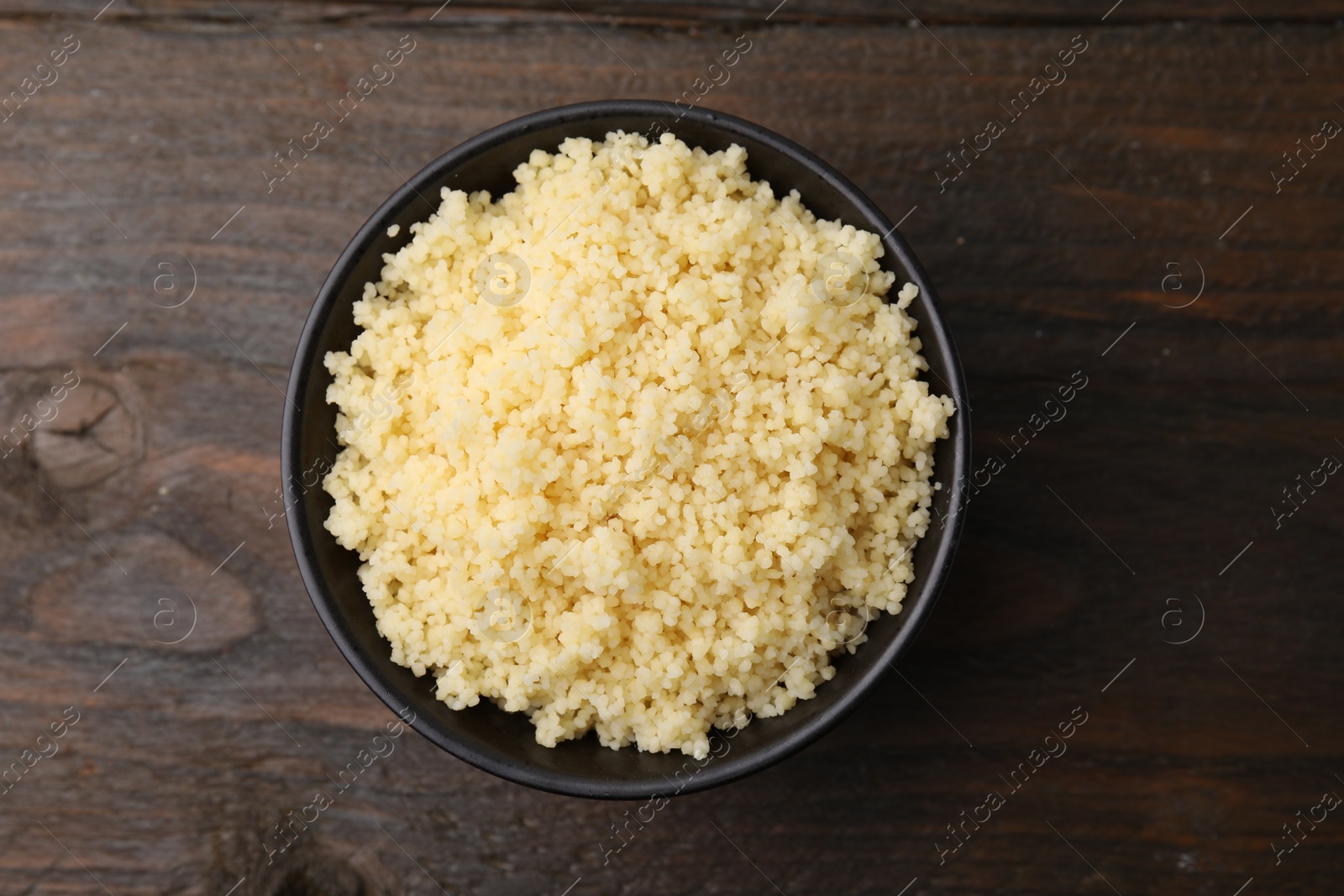 Photo of Tasty couscous in bowl on wooden table, top view