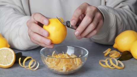 Photo of Man zesting lemon at grey table, closeup