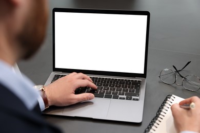 Photo of Man writing notes while working on laptop at black desk in office, closeup