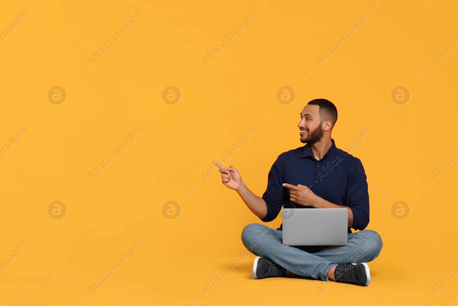 Photo of Smiling young man with laptop on yellow background, space for text