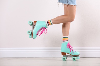 Photo of Young woman with retro roller skates near white wall, closeup