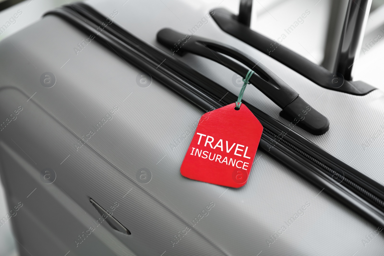 Photo of Stylish suitcase with travel insurance label on blurred background, closeup. Space for text