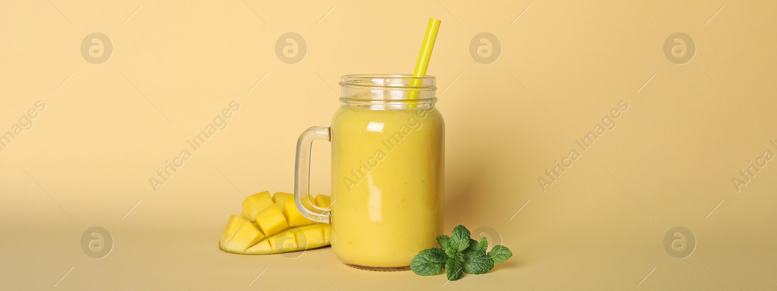 Image of Mason jar of tasty smoothie with straw, mango and mint leaves on beige background. Banner design