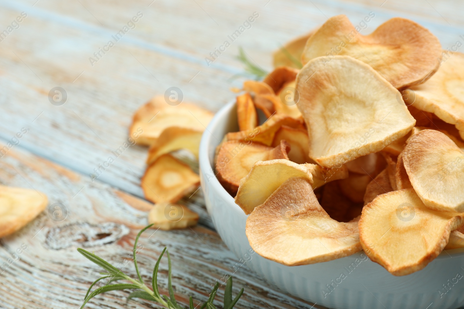 Photo of Bowl of tasty homemade parsnip chips with rosemary on old light blue wooden table, closeup. Space for text