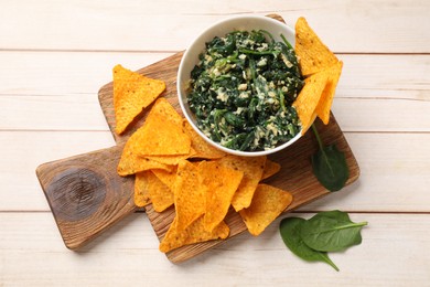 Photo of Tasty spinach dip with eggs in bowl and nachos chips on light wooden table, top view