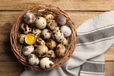 Photo of Wicker bowl with quail eggs and straw on wooden table, top view