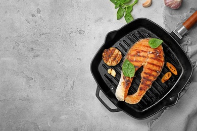 Photo of Frying pan with tasty salmon steak on grey background