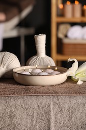 Photo of Spa composition with burning candles, lily flower and herbal bags on massage table in wellness center