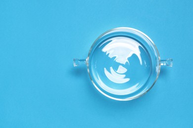 Empty glass pot on light blue background, top view. Space for text