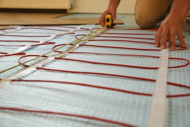 Photo of Professional worker installing electric underfloor heating system indoors, closeup