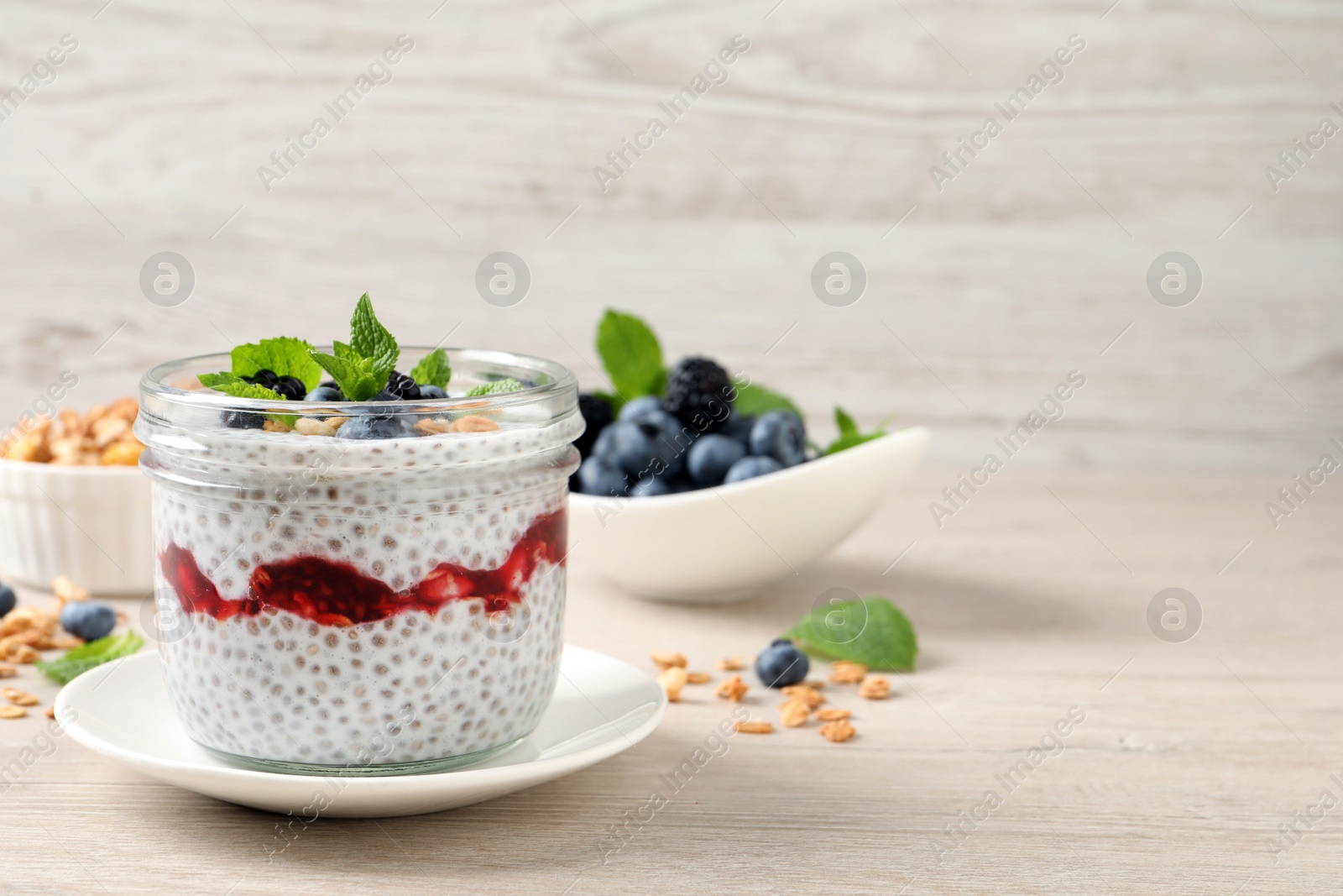 Photo of Delicious chia pudding with berries and granola on wooden table. Space for text