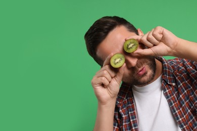 Photo of Man covering his eyes with halves of kiwi on green background. Space for text