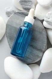 Photo of Bottle of face serum and stones on light grey background, top view